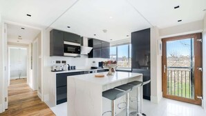 Une cuisine moderne dotée d’un îlot central, de meubles de rangement aux couleurs sombres et d’une grande fenêtre.