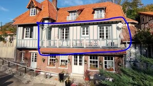 Un bâtiment à deux étages doté d’un balcon au deuxième étage, d’une cheminée et d’un petit jardin agrémenté de plantes en pot.