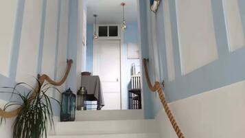 Een trap met witte treden en muren in blauw-witte strepen. Links staat een potplant en rechts een touwbalustrade.