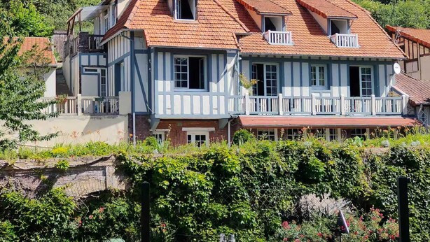 Une maison traditionnelle à deux étages, avec un toit recouvert de tuiles rouges, des boiseries blanches et de nombreuses fenêtres.