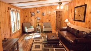 A wooden-paneled room with a leather sofa, two armchairs, a small table, and a rug.