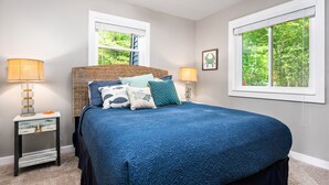 A bedroom with a large bed, two bedside tables with lamps, a window with blinds, and a framed picture on the wall. - Lake View & Access/Hot Tub/5000 Arcade Games/Pool Table/Pontoon for Rent (Kalkaska)