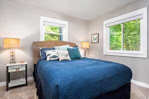 A bedroom with a large bed, two bedside tables with lamps, a window with blinds, and a framed picture on the wall.