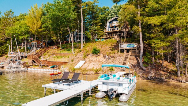 A lakeside property with a dock, lounge chairs, and a boat. - Lake View & Access/Hot Tub/5000 Arcade Games/Pool Table/Pontoon for Rent (Kalkaska)