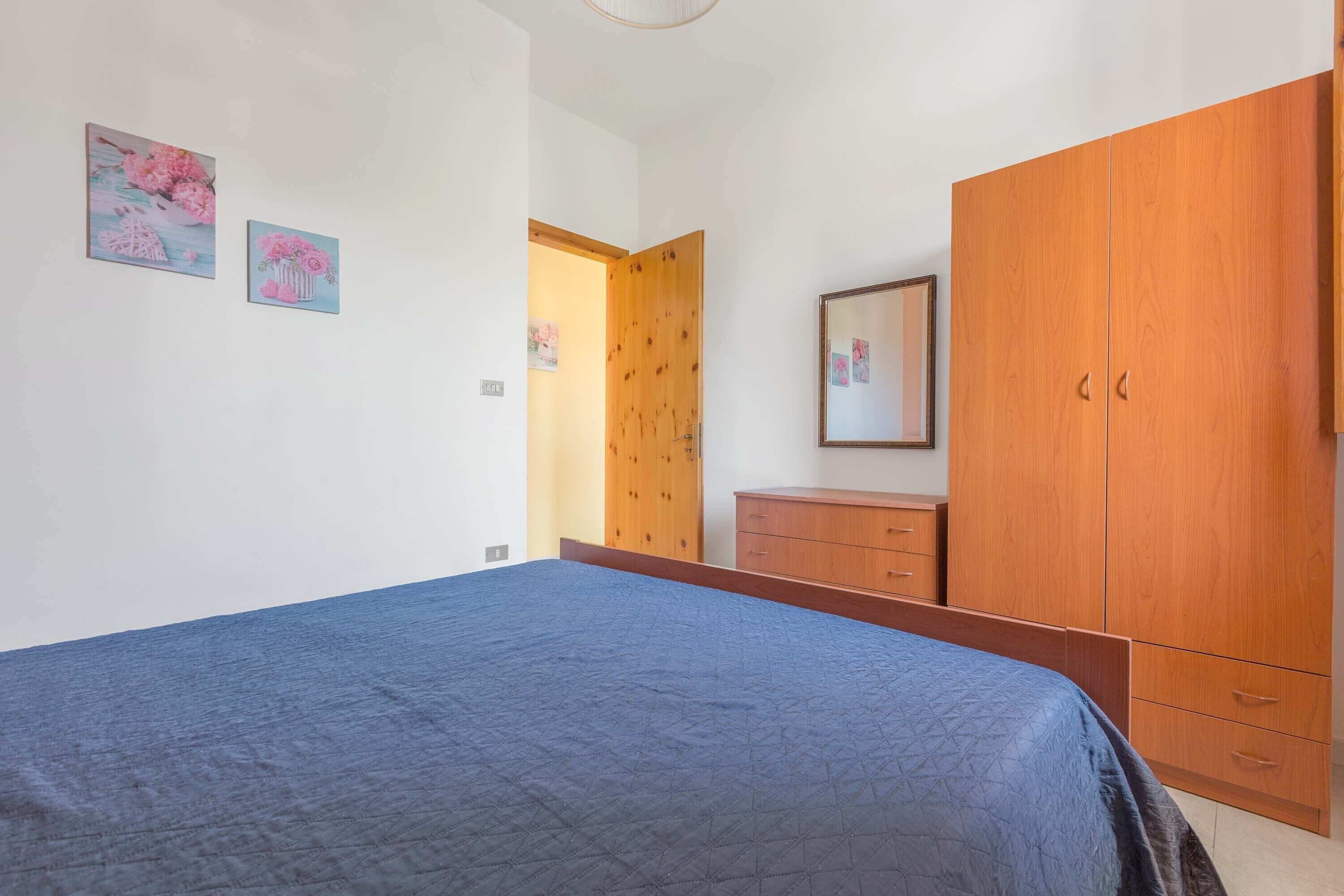 A bedroom with a bed, wooden wardrobe, and two wall-mounted pictures.