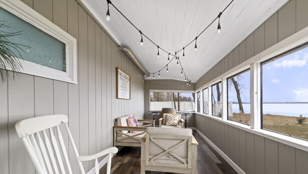 Une véranda couverte avec un plancher en bois, des chaises blanches et des guirlandes lumineuses.