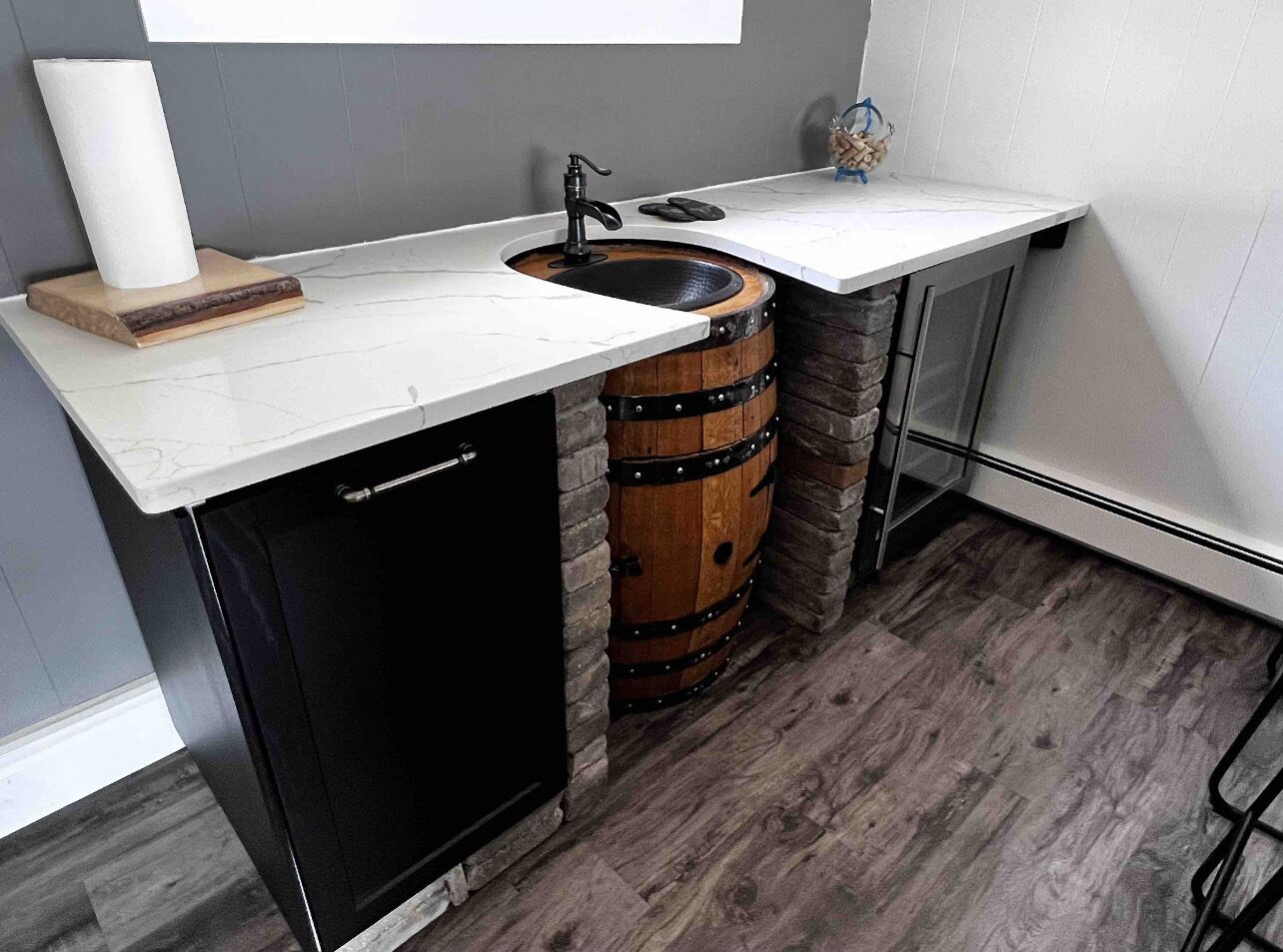 A compact kitchen with a built-in dishwasher, a wooden barrel sink, and a white countertop.