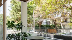 A modern outdoor seating area with a table and chairs, a potted plant, and a view of a tree-lined street. - Wynwood House Allan Poe (Mexico City)