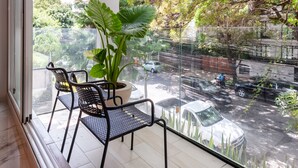 A balcony with a potted plant, two chairs, and a view of a street with cars and trees. - Wynwood House Allan Poe (Mexico City)
