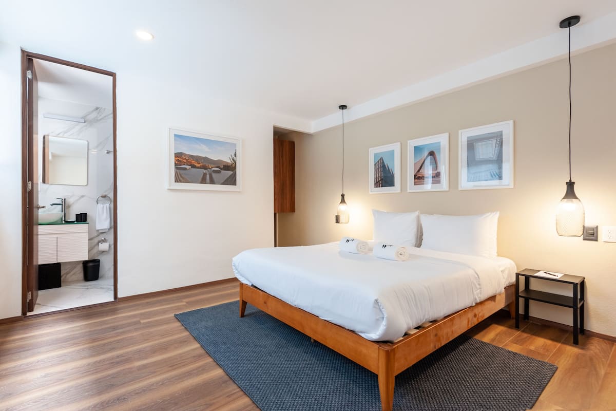 Un dormitorio moderno con una cama de madera, una mesita de noche, una lámpara de pared y cuadros enmarcados.