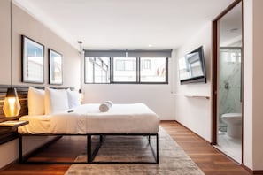 Une chambre d’hôtel moderne, équipée d’un lit, d’une télévision et d’une fenêtre donnant sur l’extérieur.