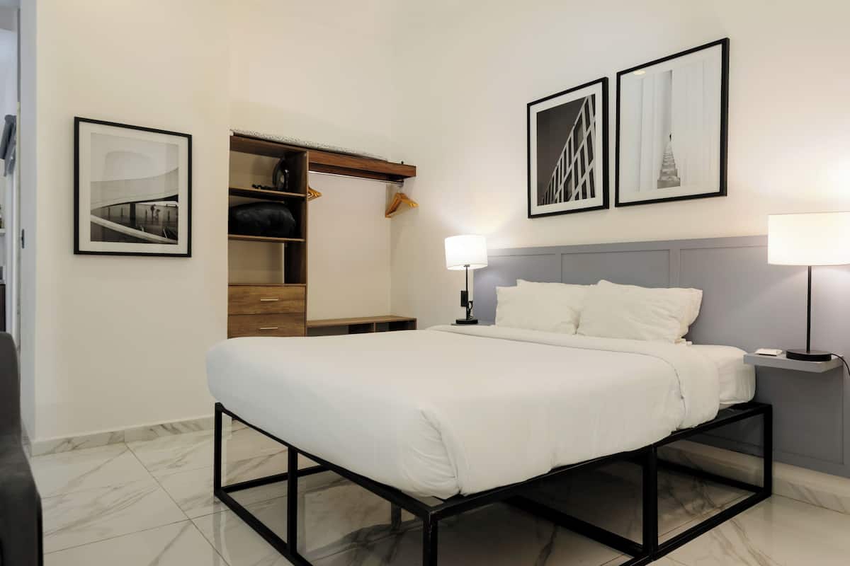 Una habitación de hotel moderna con una cama, una mesita de noche, una lámpara, un armario y dos cuadros en la pared.