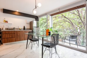 Une cuisine moderne avec une table à manger en verre, des chaises noires et une vue sur les arbres à travers de grandes fenêtres.