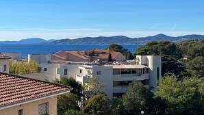 Un quartier résidentiel situé sur la côte, avec des bâtiments, des arbres et une vue dégagée sur la mer et les collines lointaines.