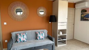 Un salon avec un canapé gris, deux miroirs décoratifs, un meuble blanc et une affiche accrochée au mur.
