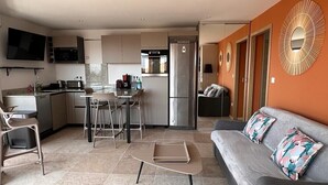 Une cuisine moderne avec un coin repas, un canapé agrémenté de coussins à motifs floraux et un téléviseur fixé au mur.