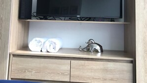 A wooden TV stand with a flat-screen TV, a black electronic device, and two rolled towels on the lower shelf. - Loft Comodo, Iluminado en Usaquen (Bogotá)