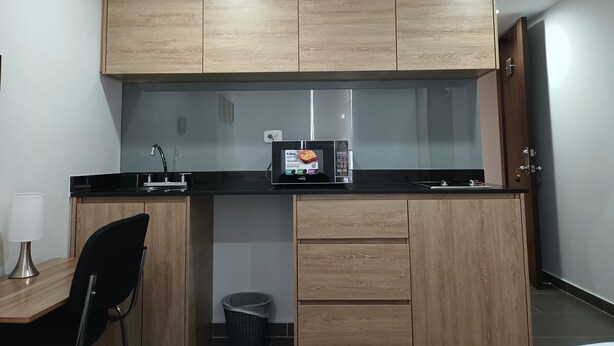 A compact kitchen with wooden cabinets, a black countertop, a microwave, a sink, and a chair. - Loft Comodo, Iluminado en Usaquen (Bogotá)