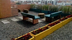 A rooftop terrace with seating areas, planters with red flowers, and a cityscape view in the background. - Loft Comodo, Iluminado en Usaquen (Bogotá)