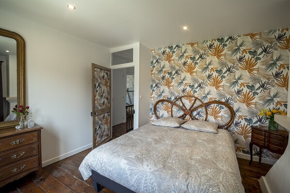 A bedroom with a large bed, a wooden headboard, a dresser, a mirror, and a floral wallpaper. - Gîte "les Rives du Dun", Charme et Calme à 4 km de la mer (Le Bourg-Dun)