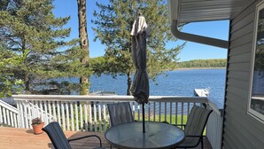A deck with a round table and chairs, a potted plant, and a view of a lake.