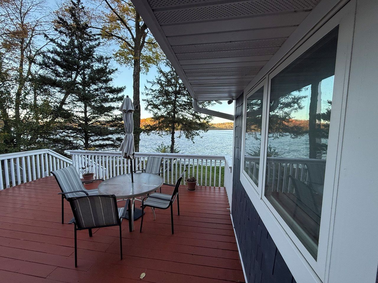 A covered outdoor deck with a table and chairs, overlooking a body of water and trees.