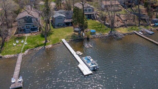 An aerial view of a lakeside property with a dock extending into the water, surrounded by houses and trees.