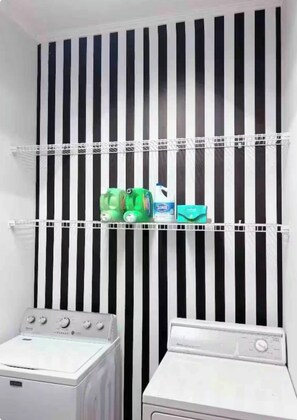 A laundry area with two washing machines and shelves with cleaning supplies. - Coastal White Cottage-Isle Of Hope in Savannah (Savannah)