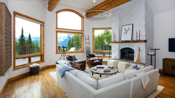 A spacious living room with a large sectional sofa, wooden flooring, and large windows offering mountain views. - Mountain Top Serenity (Big Sky)