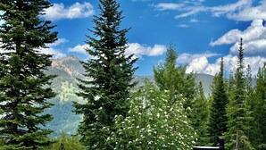 A hot tub with a mountain view, surrounded by trees and a wooden deck. - Mountain Top Serenity (Big Sky)