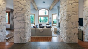 A spacious living area with a stone wall, a large window, and a sofa with cushions. - Mountain Top Serenity (Big Sky)