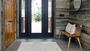 A modern entrance with a wooden wall, a black door, a bench, and a rug. - Mountain Top Serenity (Big Sky)
