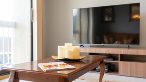 Uma mesa de madeira com velas e uma revista, uma televisão de tela plana e uma estante em uma sala de estar moderna.