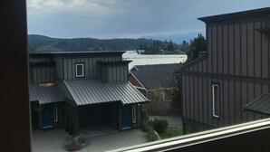 Blick aus einem Fenster eines Gebäudes mit Metallbedachung, einem überdachten Außenbereich und einer entfernten Aussicht auf ein Gewässer und Hügel.