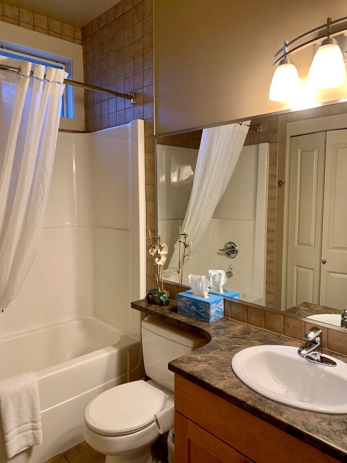 A bathroom with a bathtub, toilet, and sink. There is a towel hanging on the wall, a mirror, and a window with a curtain.