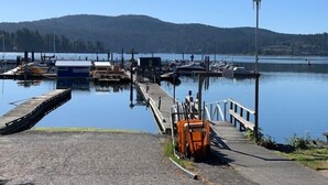 A marina with boats docked, a wooden pier, and a clear view of a lake and hills in the background. - Ocean View Townhome - Sooke Harbour Marina (Sooke)