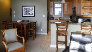 A modern kitchen with wooden cabinets, a dining area with chairs, and a bar area with stools. - Ocean View Townhome - Sooke Harbour Marina (Sooke)