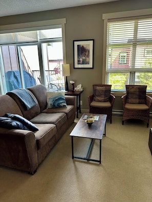 A living room with a brown sofa, two wicker chairs, a coffee table, and a framed picture on the wall.