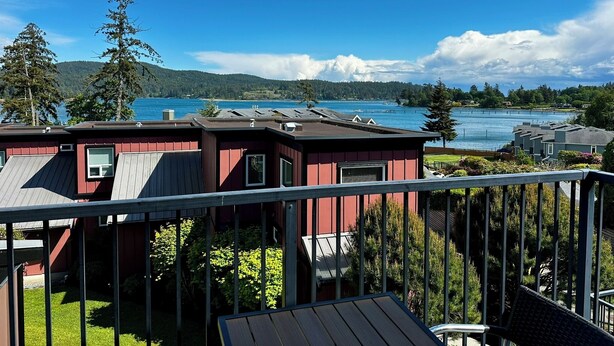 A coastal cabin with a deck, a view of the sea, and a forested hillside. - Ocean View Townhome - Sooke Harbour Marina (Sooke)