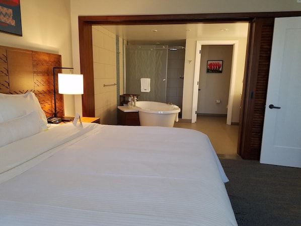 Ett hotellrum med en stor säng, en sänglampa, ett nattduksbord, ett badrum med badkar och en dusch.