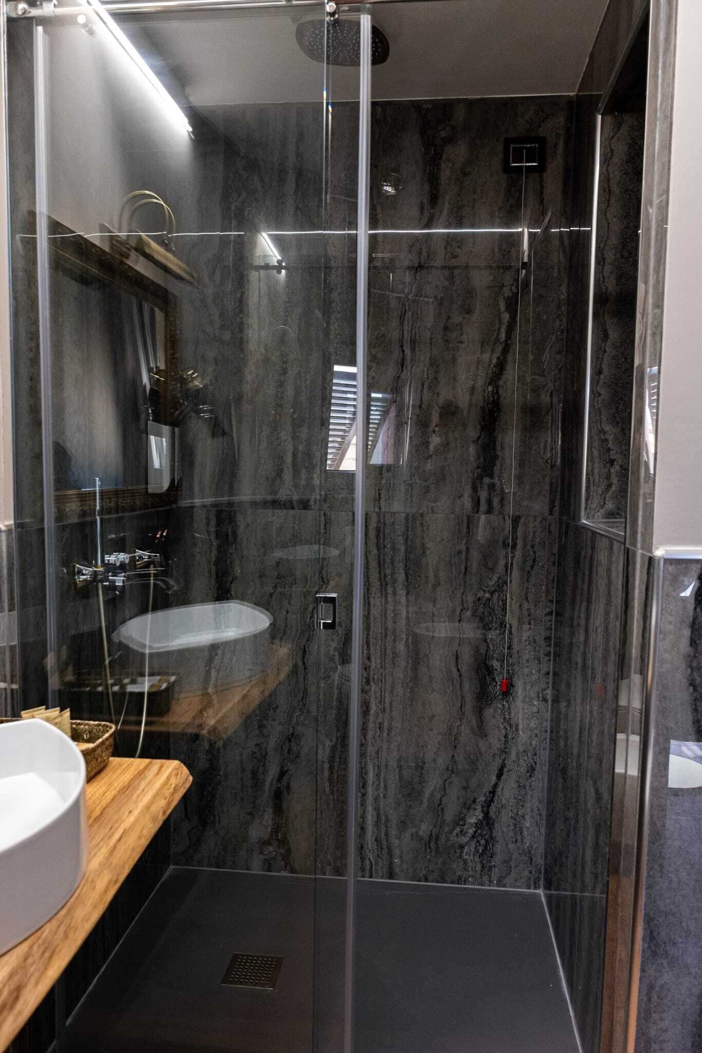 A modern bathroom with a glass-enclosed shower, a wooden vanity, and a marble backsplash.