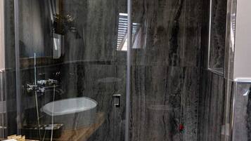 A modern bathroom with a glass-enclosed shower, a wooden vanity, and a marble backsplash.