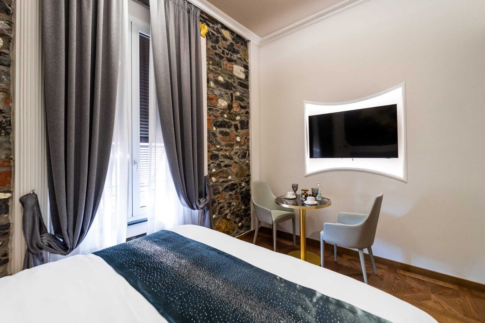 Una camera d'hotel con un letto, una parete decorata con pietra, un tavolino rotondo con sedie e una TV a parete.