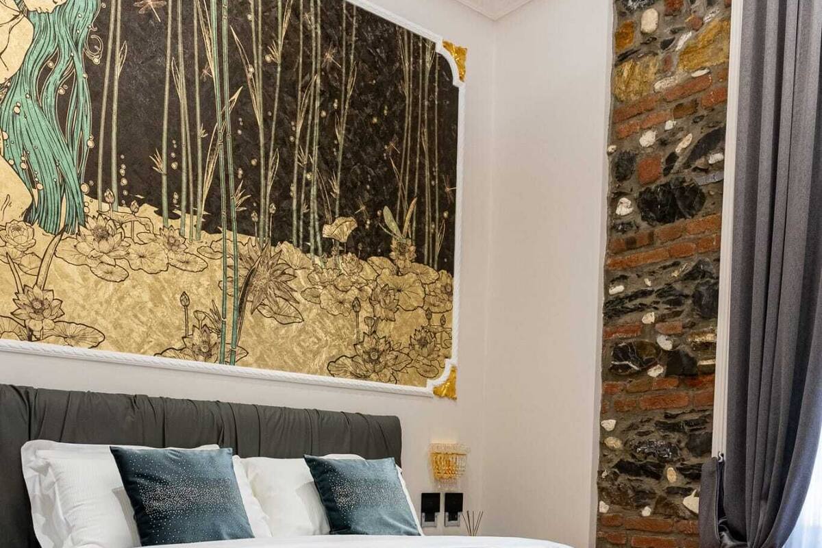 Ein Schlafzimmer mit einem großen Bett, einem runden Hocker, einer Steinwand und einem Wandgemälde.