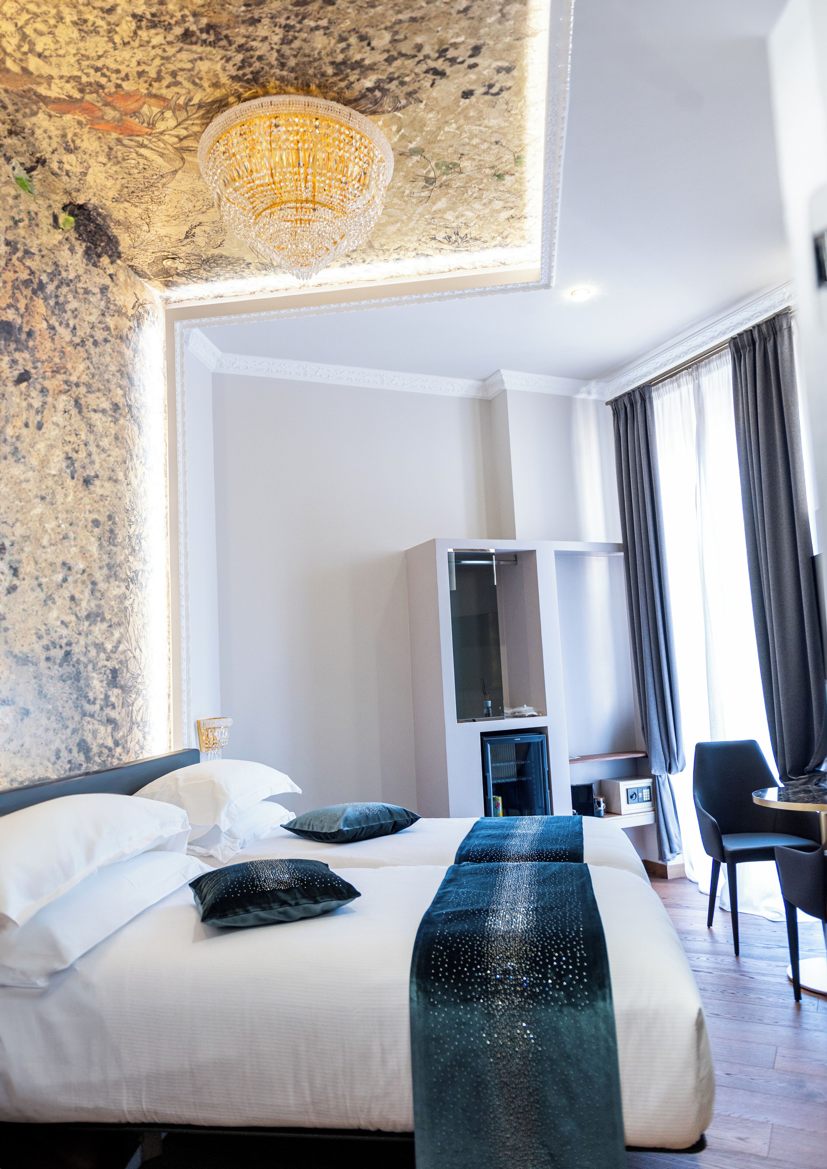 A hotel room with a large bed, a wardrobe, a desk, and a chandelier.
