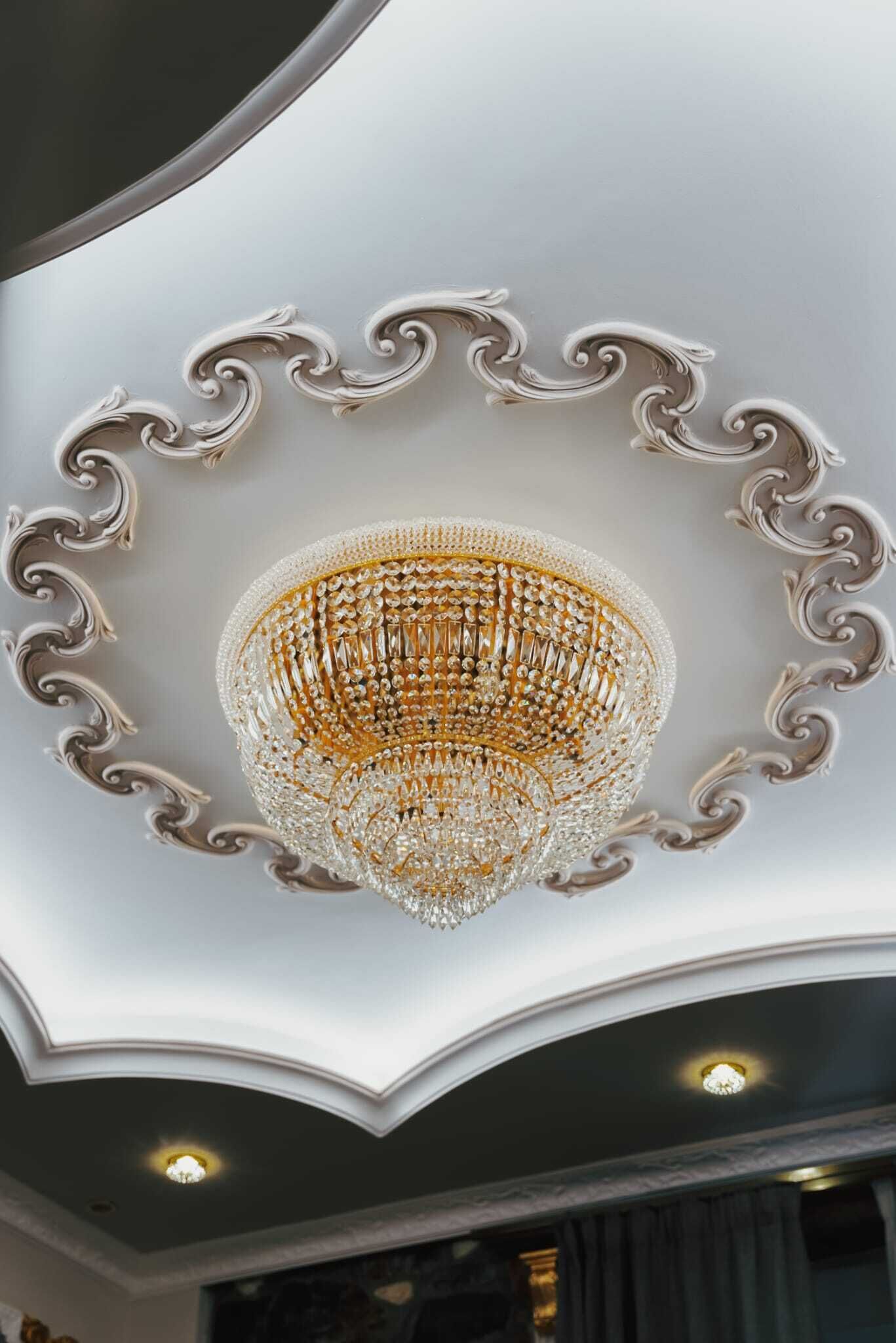Un magnifique lustre, orné de motifs complexes en cristal, est suspendu sous un plafond décoratif agrémenté de moulures travaillées.