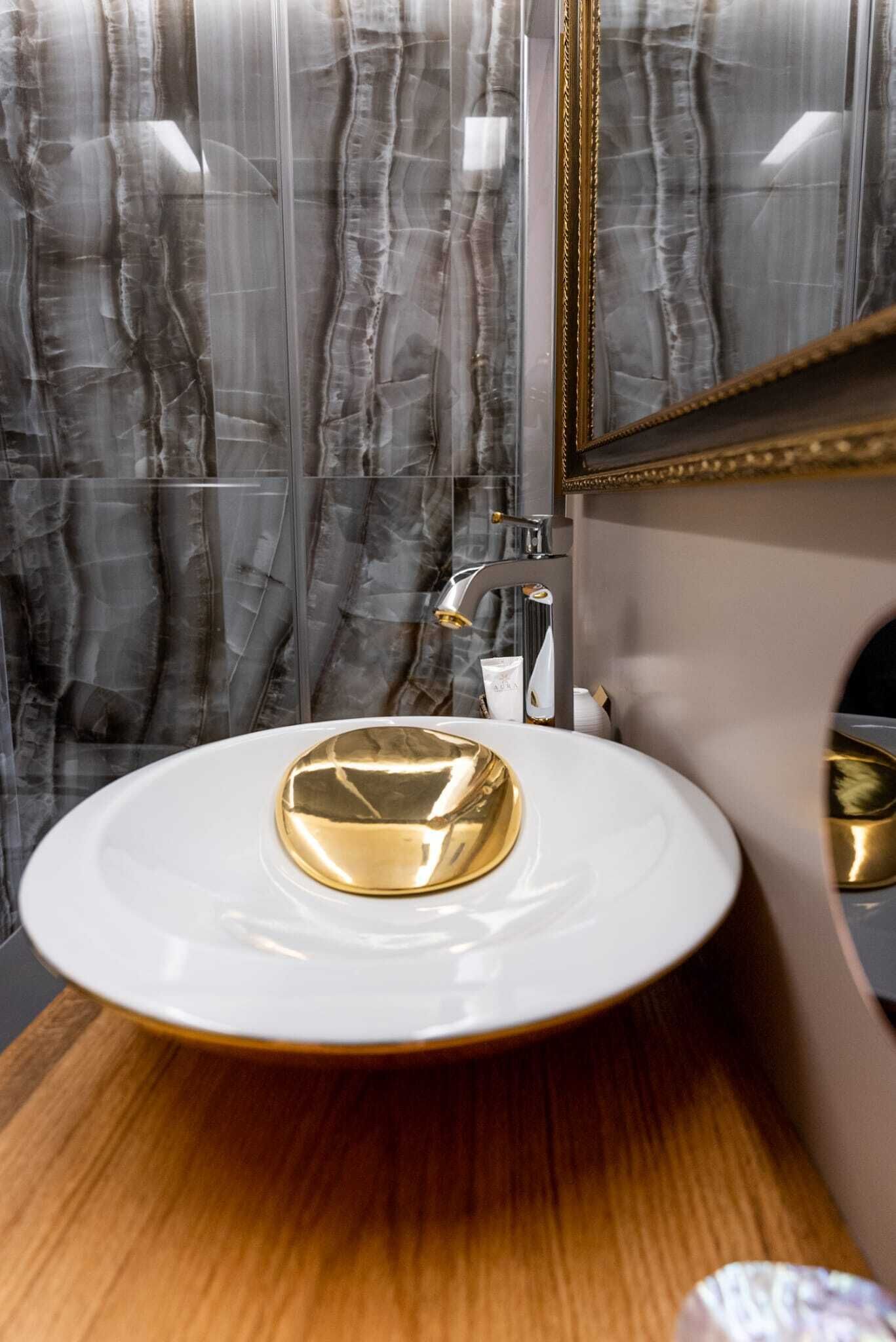 Une salle de bain avec un meuble-lavabo en marbre, un lavabo de couleur dorée et un miroir avec un cadre doré.