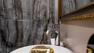 Une salle de bain avec un meuble-lavabo en marbre, un lavabo de couleur dorée et un miroir avec un cadre doré.