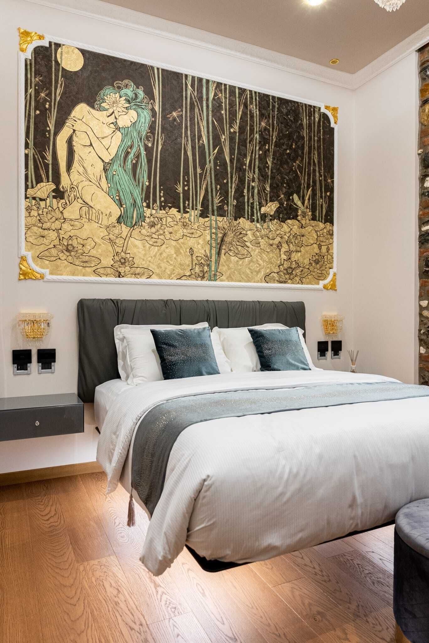 A bedroom with a large bed, a nightstand, a wall-mounted lamp, and a large painting above the bed.