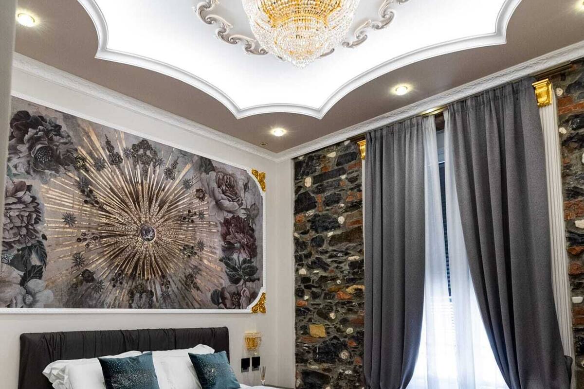 Ein Schlafzimmer mit einem großen Bett, einer Kristallleuchtre, einer Steinwand und einem großen Blumenbild.